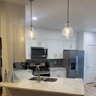 Modern kitchen with white cabinets, stainless steel appliances, and pendant lights over a countertop.