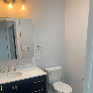 Bathroom with blue vanity, white countertop, white and gold fixtures, and toilet.