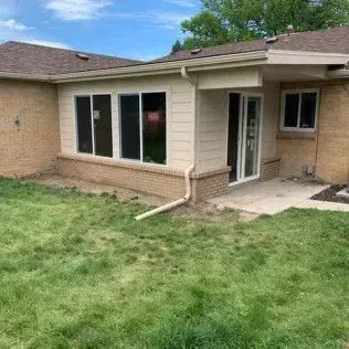 Exterior of a house with an attached sunroom and backyard. Green grass, brick and siding visible.