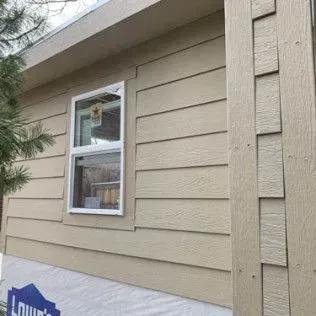 Beige siding on a building with a window and trim. The foundation is covered with a Lowe's tarp.