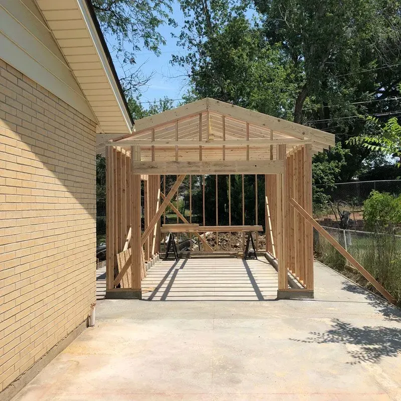 Wooden frame of a carport under construction, attached to a brick building.