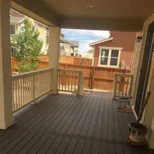 Covered porch with wood flooring, railing, and view of other houses.