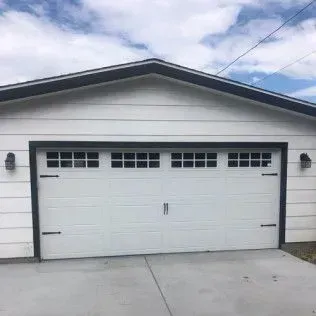 White garage with black trim and windows, a concrete driveway, and a cloudy sky.