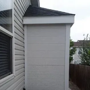Exterior wall with light gray horizontal siding, white trim, and a dark shingled roof.