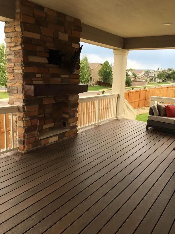 Covered outdoor deck with brown composite decking, a stone fireplace, and a couch.