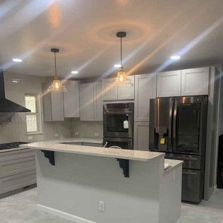 Gray kitchen with island, stainless steel appliances, pendant lights, and cabinetry.