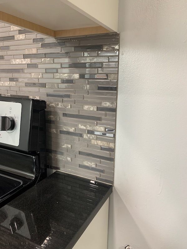 Gray and silver tile backsplash next to a white wall and a black countertop, near a stove.