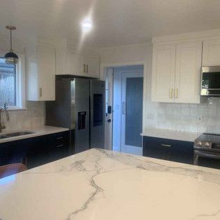 Kitchen with white and dark cabinets, marble countertop, stainless steel appliances, and a door.