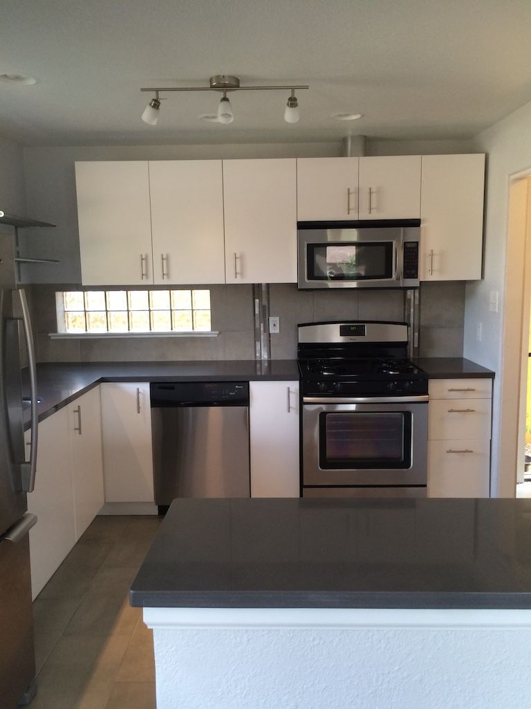 Modern kitchen with white cabinets, stainless steel appliances, dark countertop, and an island.