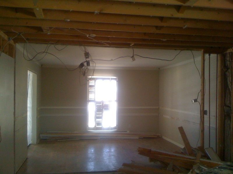 Interior room under renovation, with exposed ceiling beams, unfinished walls, and a window.