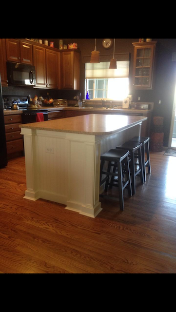 Kitchen island with stools, wood cabinets, and wood flooring. Island has white base, light countertop.