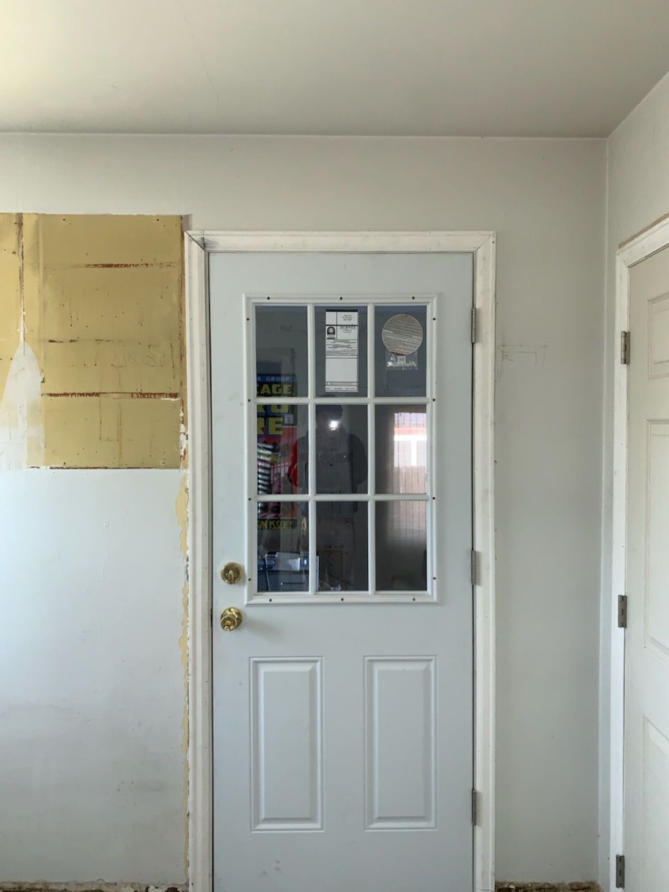 White door with glass pane, set in a light grey-painted room, with visible construction.