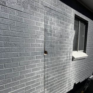 Gray brick exterior wall with a window and vertical crack.