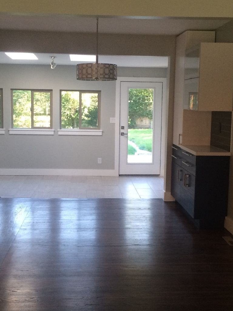 Interior view of a renovated home with hardwood floors, light gray walls, and a view of the backyard through a door.