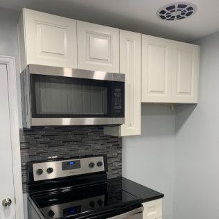 Stainless steel microwave above a black stove against a gray-tiled backsplash and white cabinets.