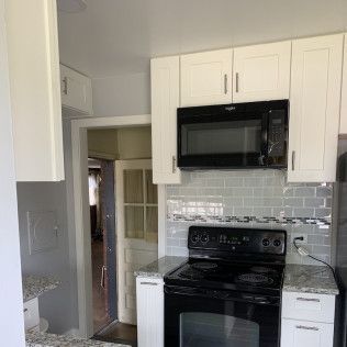 Kitchen with white cabinets, black microwave and stove, gray tiled backsplash.