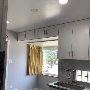 Kitchen with upper cabinets, window with yellow curtains, and a sink.