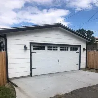 White garage with black trim and a concrete driveway under a blue sky.