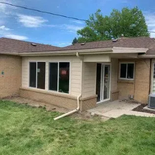 Exterior of a house with a sunroom, brick base, and a grassy yard on a sunny day.