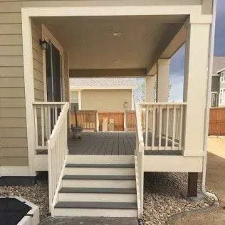 Covered deck with stairs, white railing, and columns. A back yard is visible in the background.
