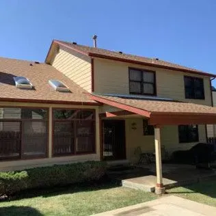 Two-story tan house with brown roof and trim; sunny day.