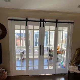 Four-panel French doors, white and glass, hang on black sliding hardware. Interior view of a sunny room.