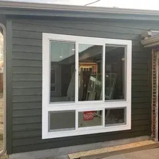 White-framed, multi-pane window installed in a green-sided building. Interior reflects construction materials.