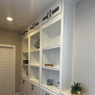 Built-in white bookshelves with black hardware in a hallway, some items on shelves.