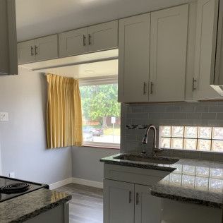 Kitchen with light gray cabinets, granite countertops, and a window with a yellow curtain.