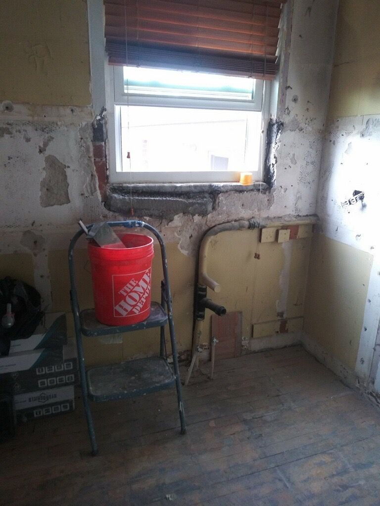 Interior renovation: Red bucket and tools on a step ladder near a window. Walls stripped of material.