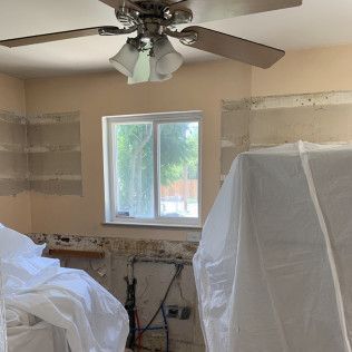 Kitchen renovation in progress, window, covered appliances, beige walls, exposed wiring, and a ceiling fan.