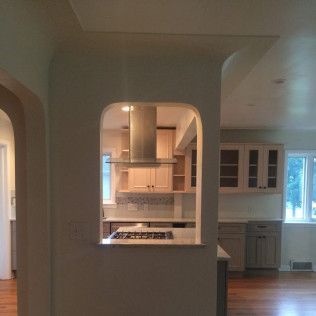 Archway view of a kitchen, including stove, cabinets, and a vent hood.