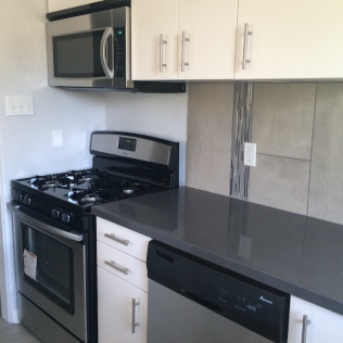 Modern kitchen with stainless steel appliances, white cabinets, and gray countertops.