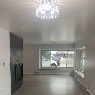 Empty, freshly painted living room with large window, fireplace, and modern light fixture.