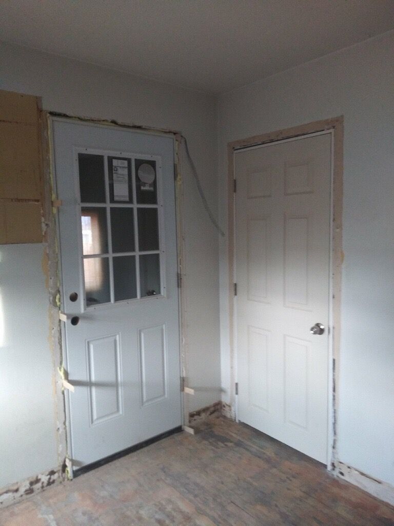 Two white doors in a room with damaged walls and floor, one with glass panes, the other solid.