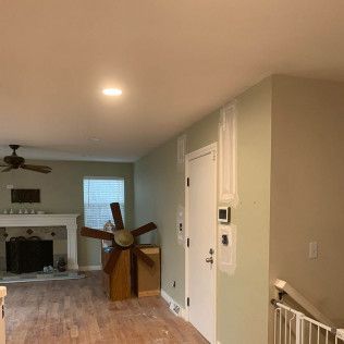 Living room with fireplace, fan, windmill prop, and a door, painted walls, light wood floors.