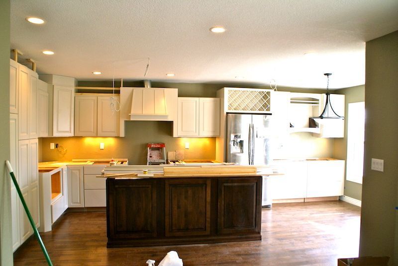 Kitchen under construction, with white cabinets, dark wood island, and wood flooring.