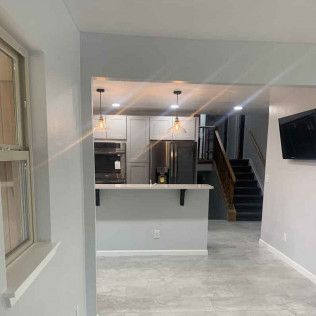 Interior view of a modern kitchen and living space, with gray cabinets and flooring.