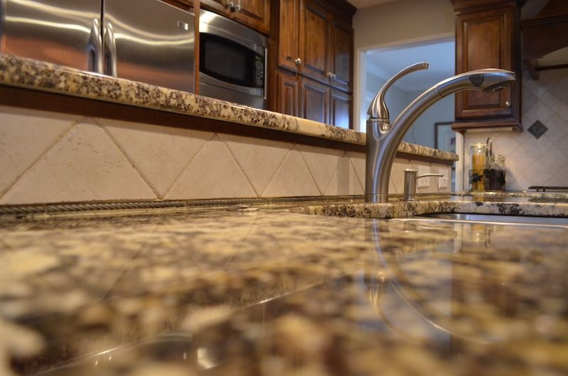 Close-up view of a kitchen countertop with a granite surface, faucet, and cabinetry.