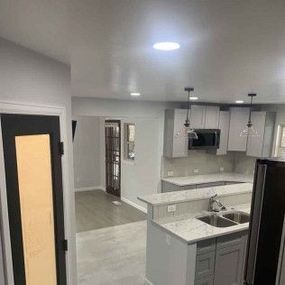 Kitchen with gray cabinets, island, and overhead lighting. Dark door in foreground.