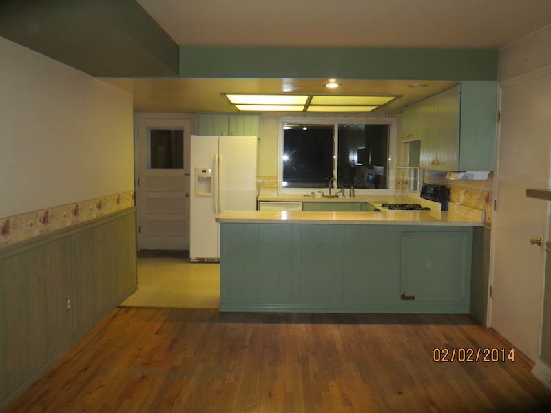Kitchen with light green cabinets, light wood floor, and a window with night view.