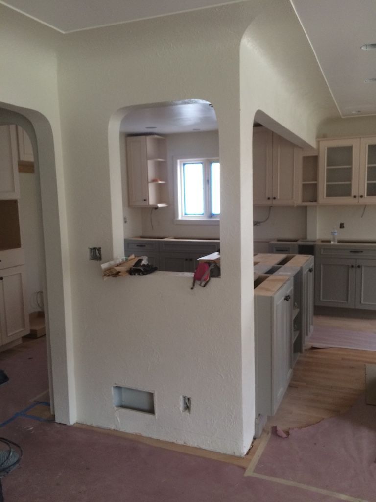 Interior view of a kitchen under renovation, featuring cabinetry, an archway, and a pass-through opening.
