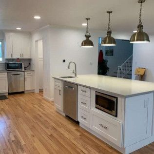White kitchen with island, stainless steel appliances, pendant lights, and hardwood floors.