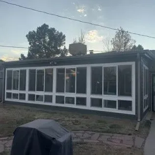 Sunroom addition with white frames and dark siding against a cloudy sky.