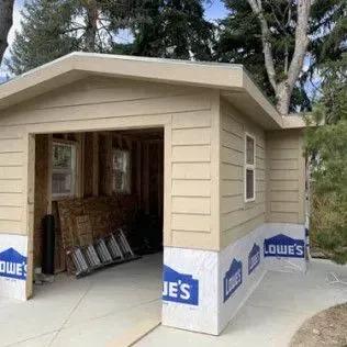 A tan-colored shed-like structure with an open garage door; Lowes paper is attached to the bottom.