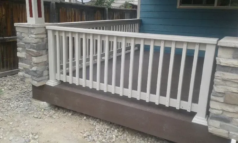 A white-railed porch with stone columns and a brown base, against a blue house.