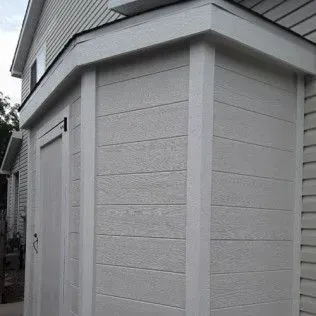 Gray shed with white trim, door, and horizontal siding, built against a house.