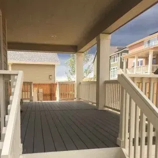 Covered porch with gray decking, white railing, and view of neighboring houses.