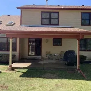 Tan two-story house with a covered patio, featuring brown trim and a green lawn.