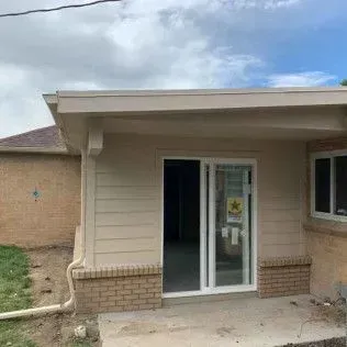 Beige-sided addition with sliding glass door and brick accents, under a light-colored roof
